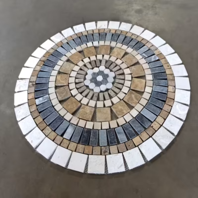 Rosace en marbre et travertin, AL-2439, composée de tesselles de différentes tailles et couleurs (blanc, marron et noir), vue de biais sur fond gris.